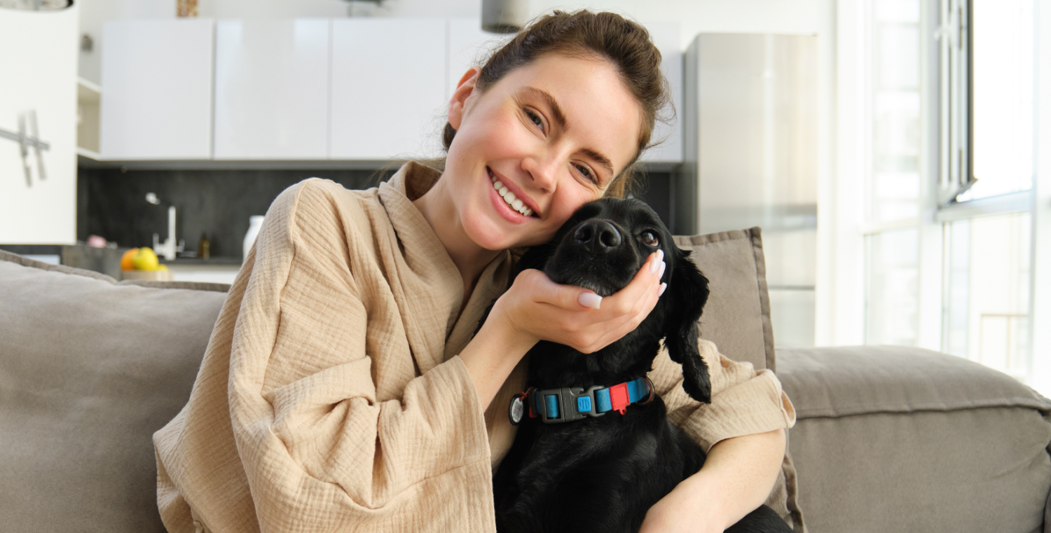 Eine Frau sitzt mit Ihrem Hund auf dem Sofa in ihrer Wohnung, wo sich Allergene befinden.