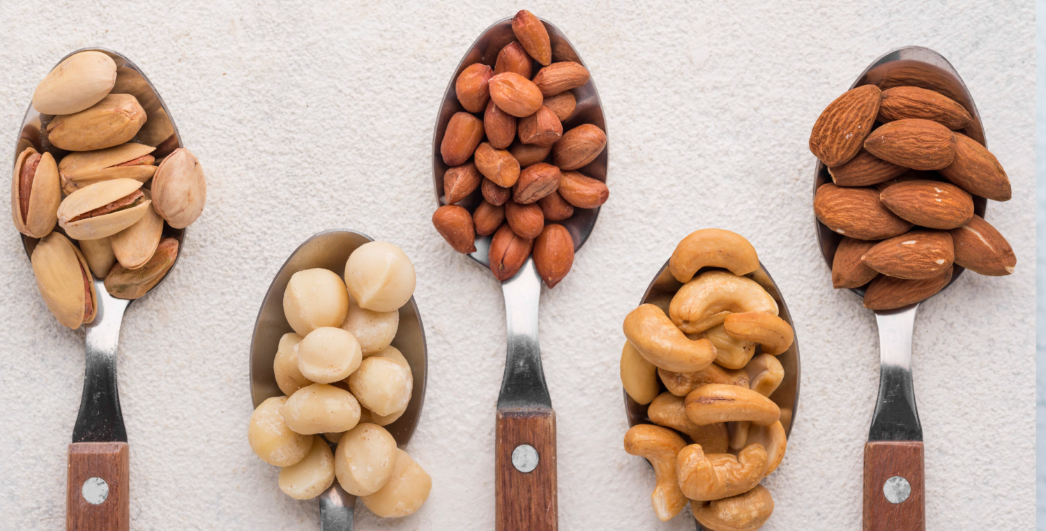 Auf 5 Esslöffeln sind jeweils eine Portion von Nüssen aufgehäuft: Pistazien, Macadamia, Erdnüsse, Cashews und Mandeln.