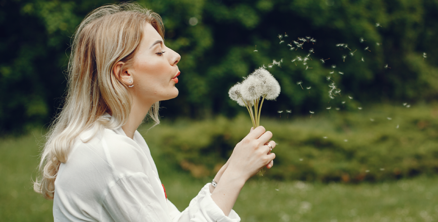Eine Frau pustet auf Löwenzahn-Pollen.