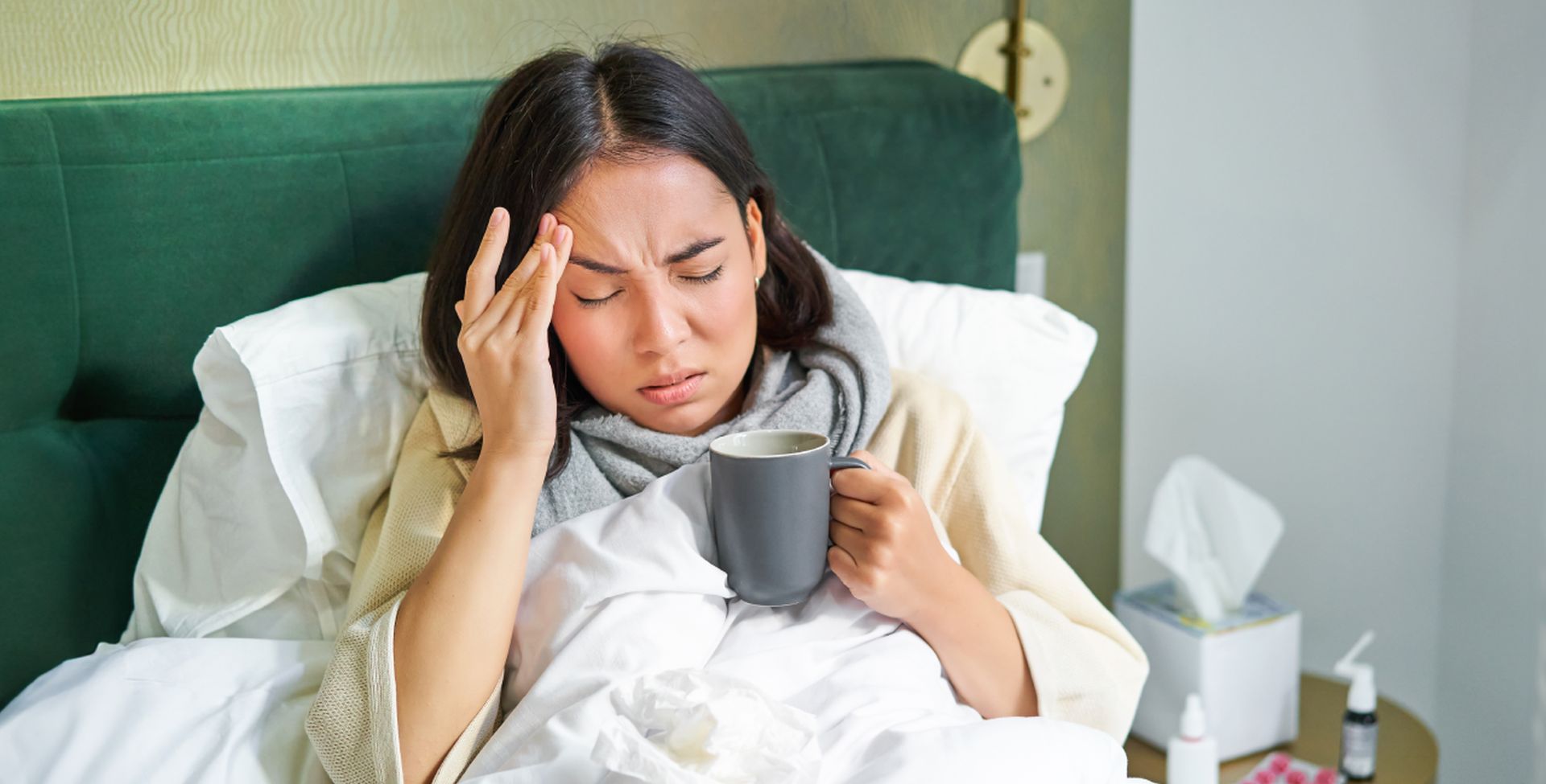 Eine Frau ist mit Tee im Bett, weil ihr schwaches Immunsystem sie öfter krank werden lässst.