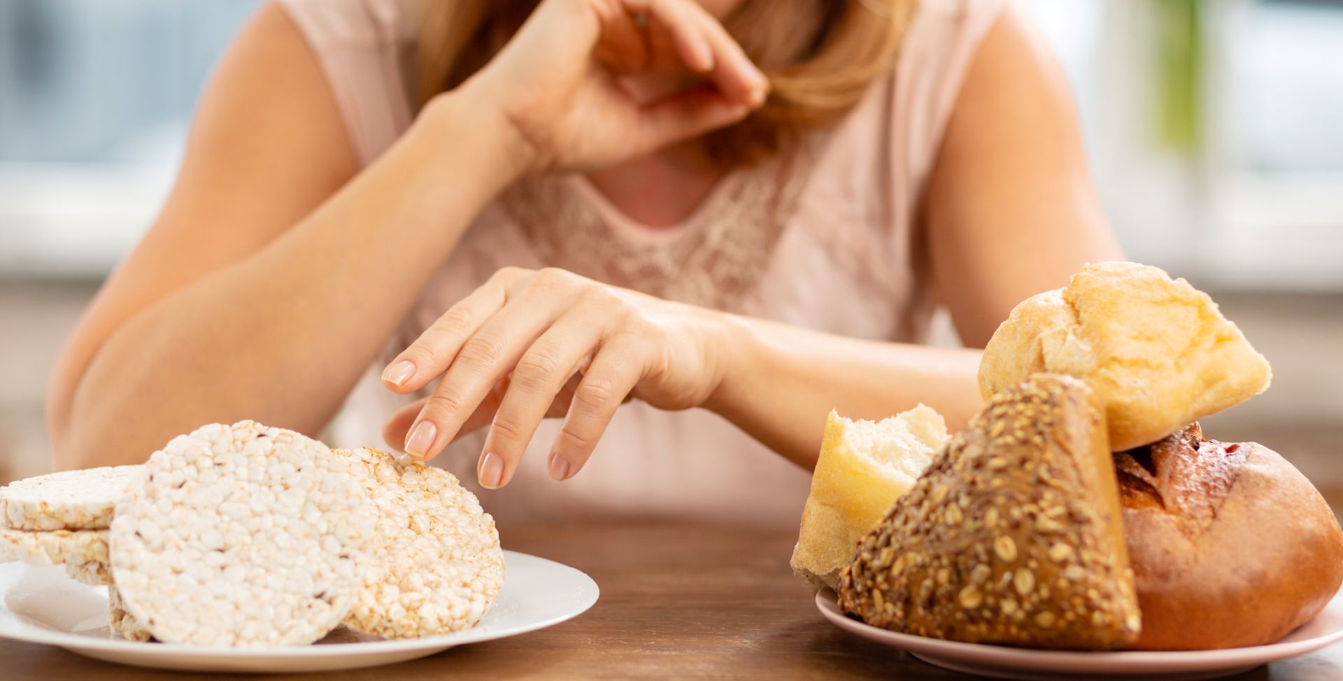 Eine Frau mit Glutenunverträglichkeit vor einem Teller mit Reiswaffeln und einem Teller mit Brot.