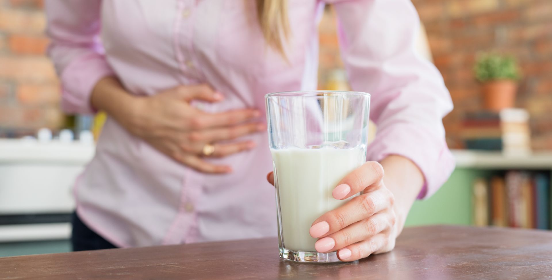 Eine Frau mit Laktoseintoleranz hält ein Glas Milch und ihren Bauch.