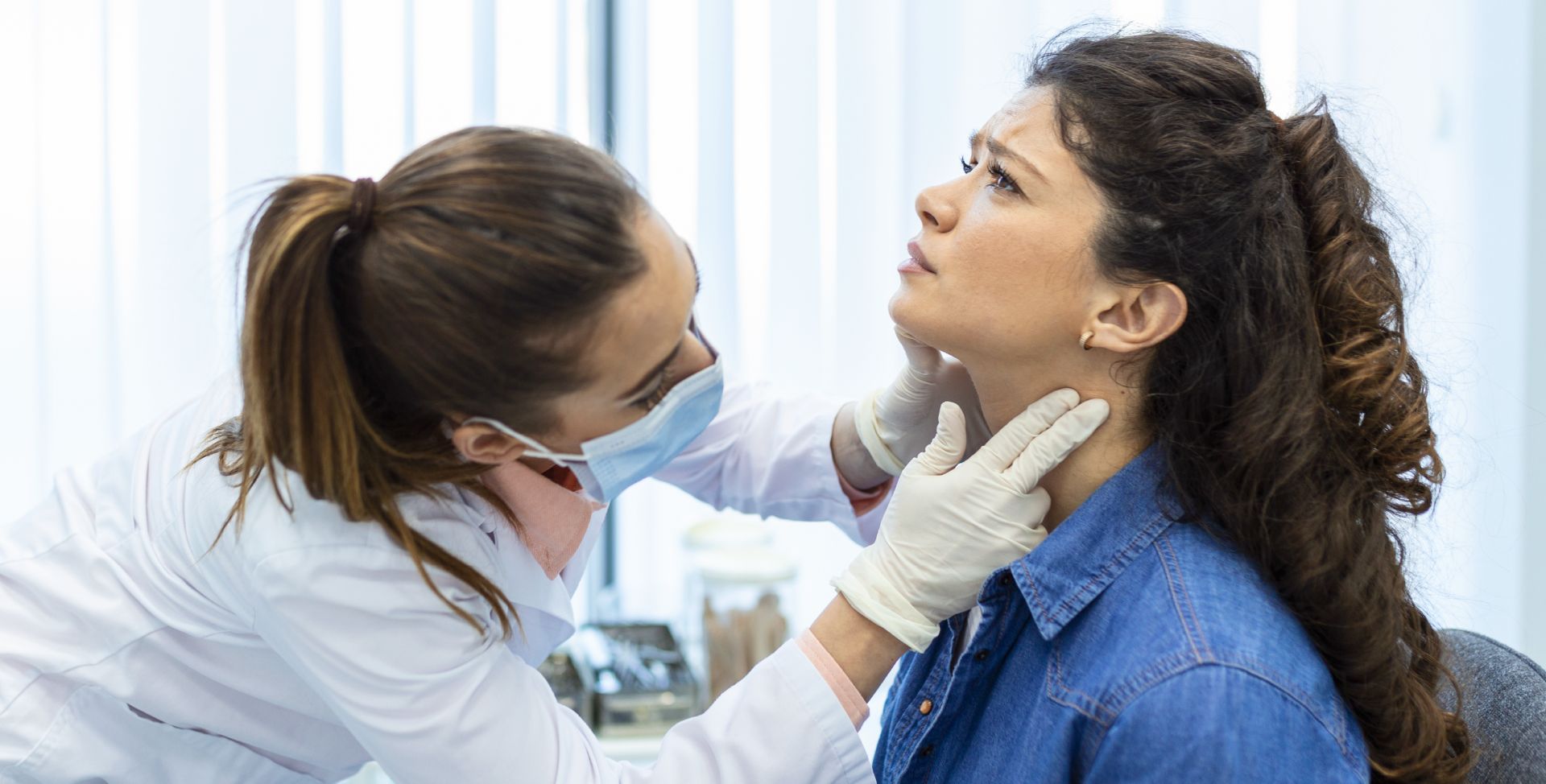 Eine Ärztin untersucht den Hals einer Patientin auf eine Schilddrüsenunterfunktion.