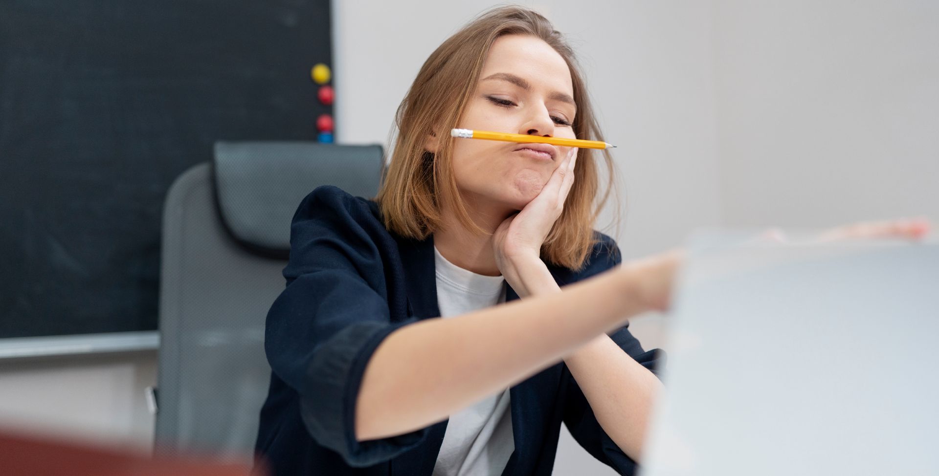 Eine Frau balanciert im Büro einen Stift auf ihrer Lippe, eine Folge von Konzentrationsstörungen durch vererbbares ADHS.