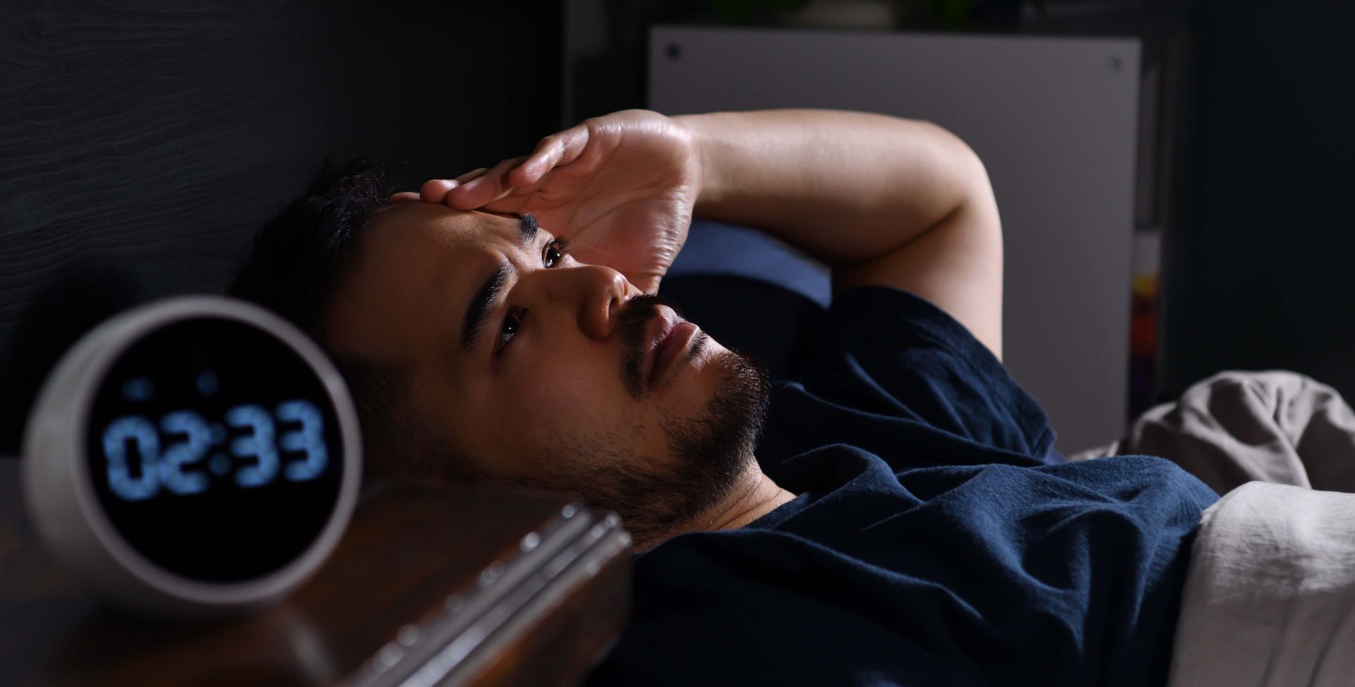 Ein Mann liegt nachts mit Insomnie wach im Bett.