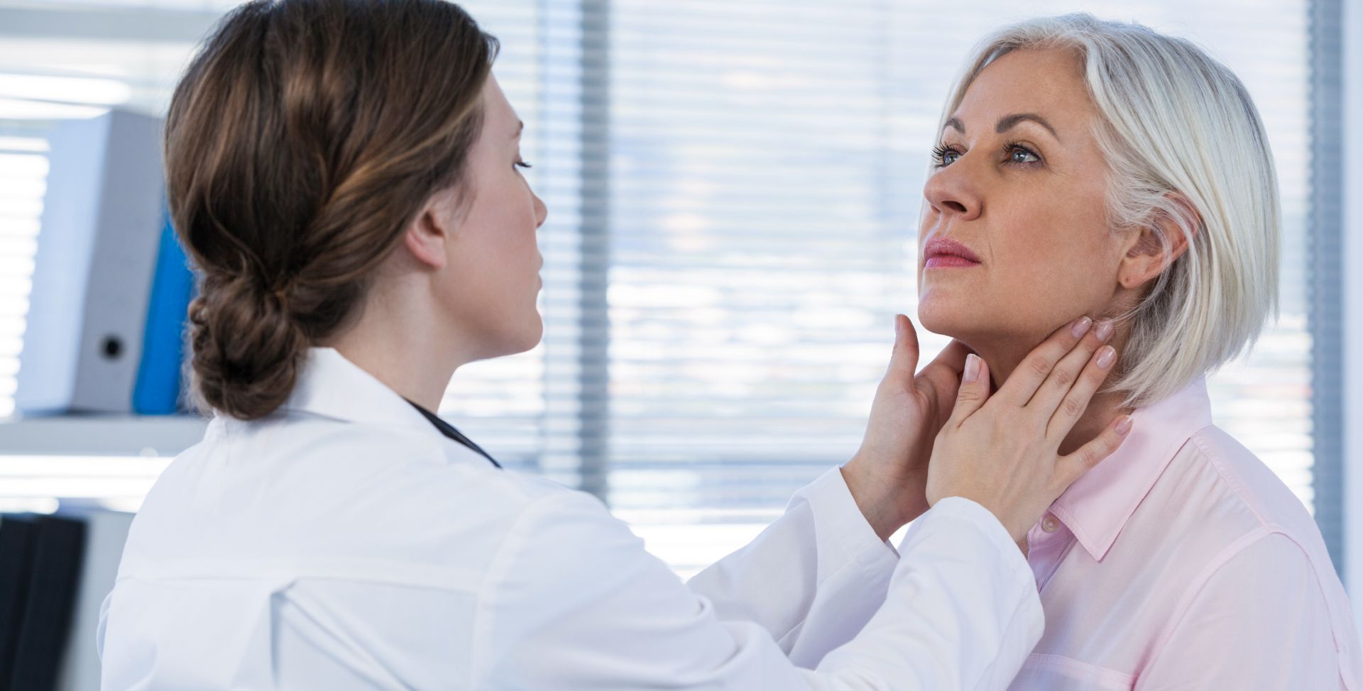 Eine Ärztin untersucht den Hals einer Person auf Anzeichen einer Schilddrüsenüberfunktion.