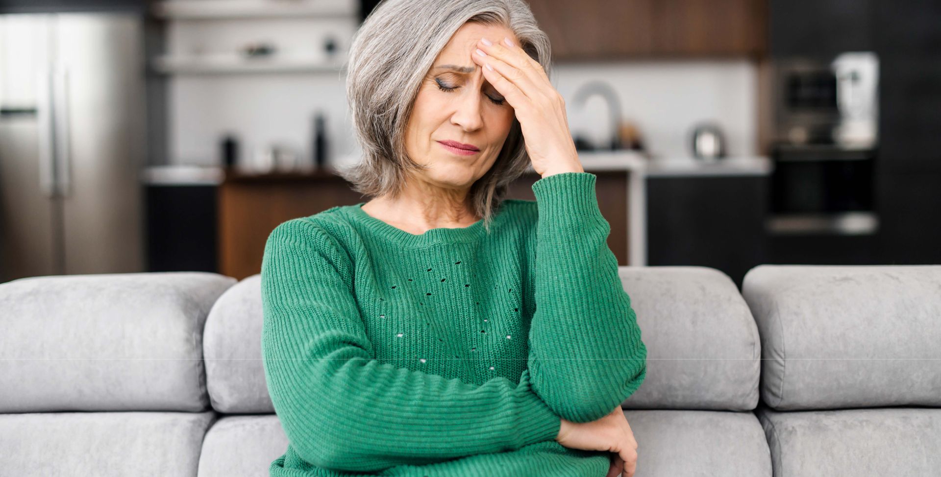 Eine ältere Frau hält sich die Hand an den Kopf, weil sie Beschwerden der Wechseljahre erlebt.