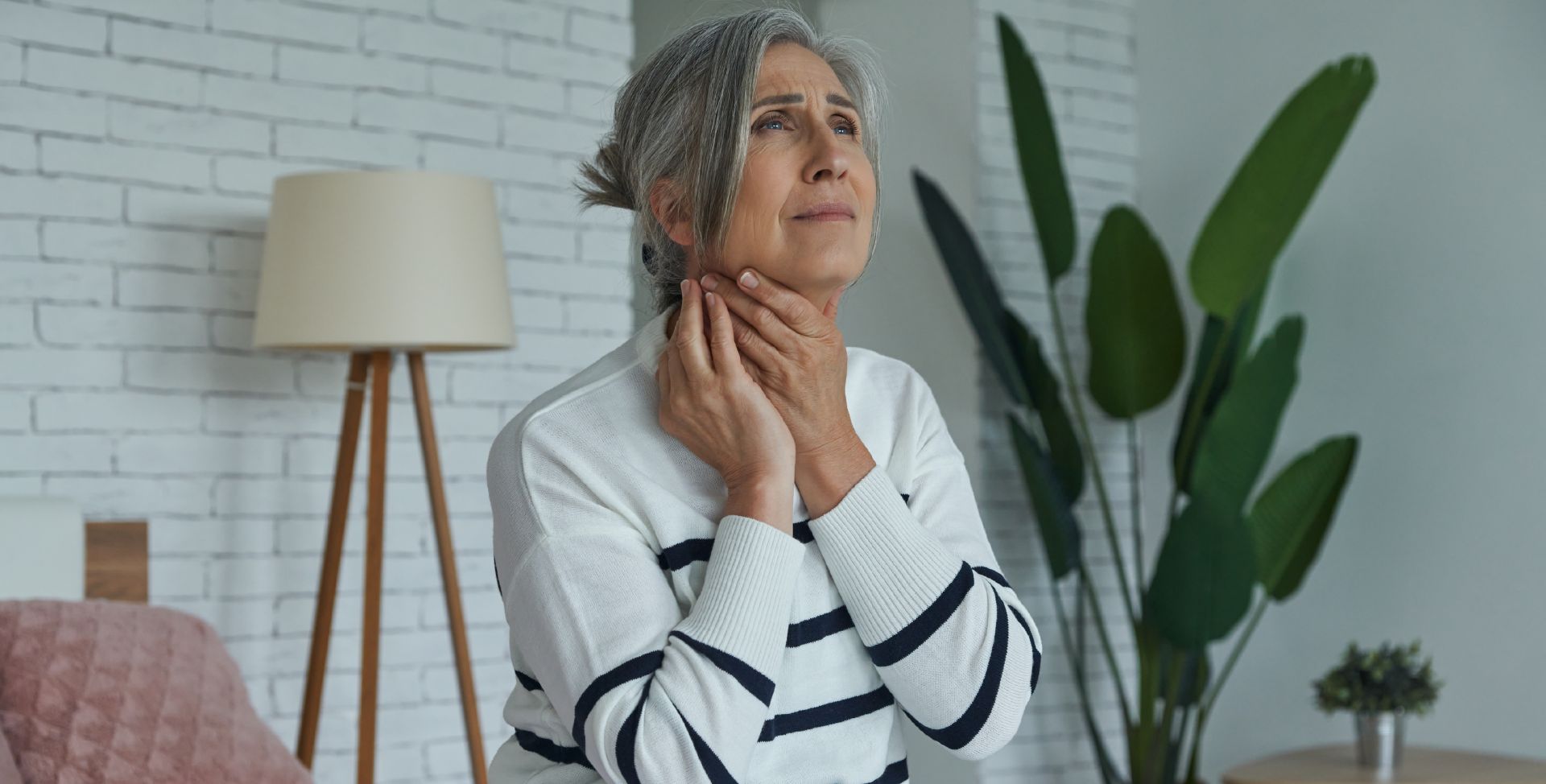 Eine Frau fasst sich an den Hals. Sinnbild für die Schilddrüsenerkrankung Hashimoto-Thyreoiditis.