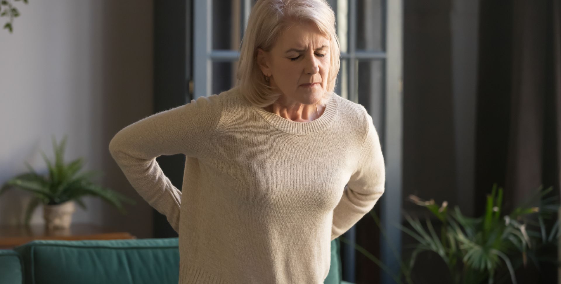 Eine gebückte Frau mit Rückenschmerzen als Sinnbild für Osteoporose.