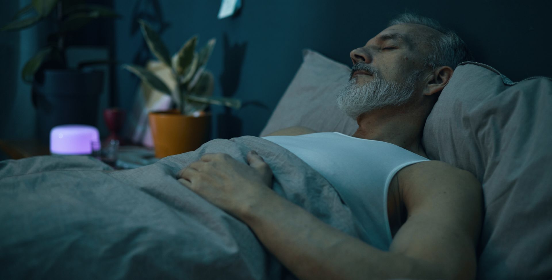 Ein Mann schläft nachts im Bett. Sinnbild für das Schlafhormon Melatonin.