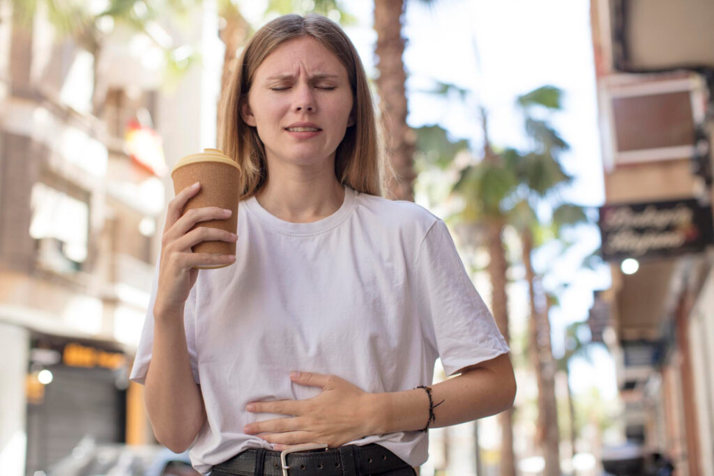 Eine Frau mit Koffeintoleranz mit Bauchschmerzen und Kaffeebecher in der Hand.