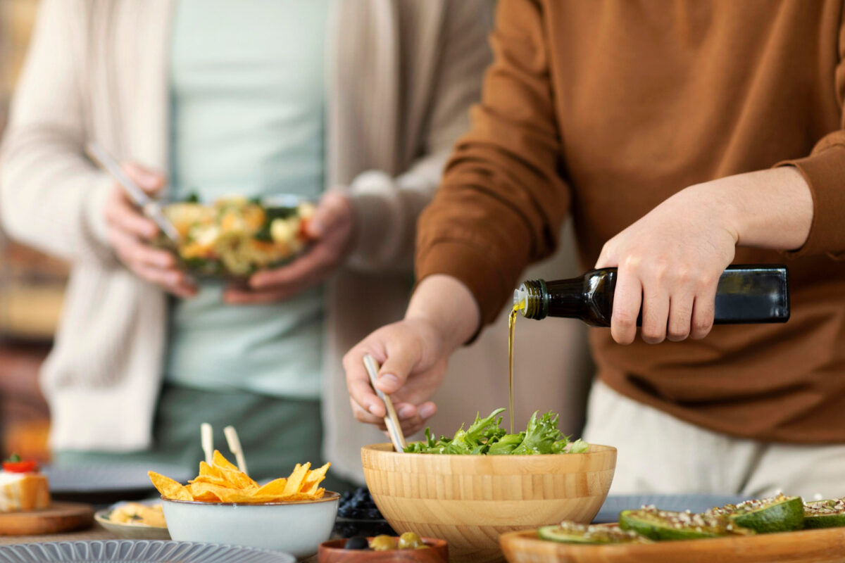 Jemand gießt Olivenöl auf einen Salat – gesunde Fette für den Körper.