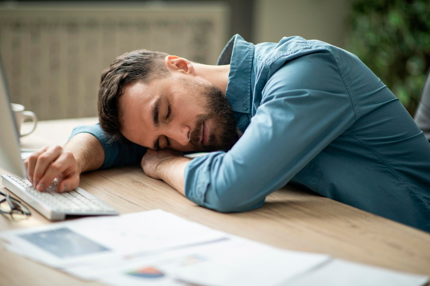Ein Mann schläft wegen ständiger Müdigkeit am Schreibtisch.
