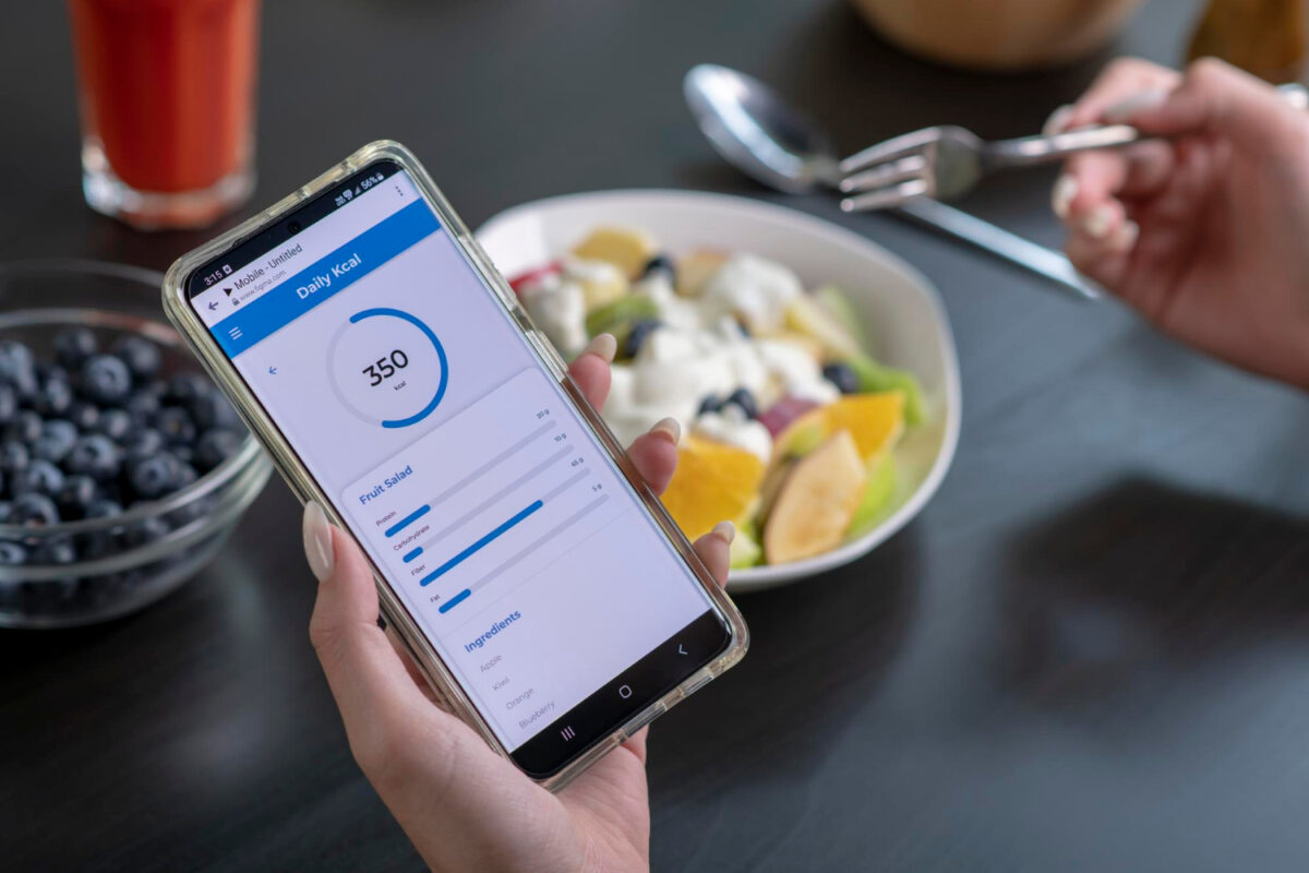 Eine Person gibt die Kalorien der Mahlzeit in ihr Handy ein, nachdem der Kalorienzähler den Kalorienverbrauch des Körpers ermittelt hat.