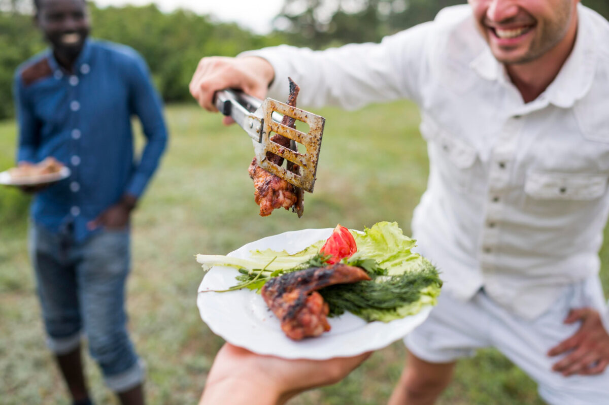 Beim Grillen legt ein Mann Fleisch auf einen Teller mit wenig Kohlenhydraten, wie bei der Atkins-Diät vorgesehen.